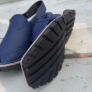 May include: A pair of blue leather sandals with a black rubber sole. The sandals have a strap that goes around the ankle and a toe loop.