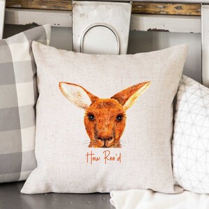 Puede incluir: Una almohada de lino beige con una ilustración de acuarela de la cara de un canguro. El texto "How Roo'd" está impreso en naranja debajo del canguro.