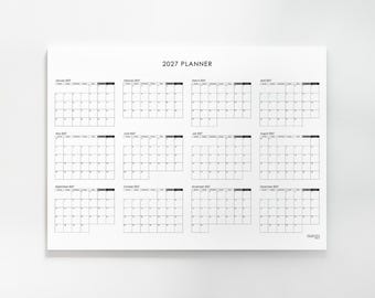 May include: A white 2027 planner wall calendar featuring a clean, black grid layout for all twelve months of the year. Each month is clearly labeled with its name and year, organized into a structured table format with days of the week listed.