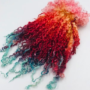 May include: A long strand of curly yarn dyed in a gradient of pink, orange, red, blue, and green.