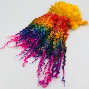 May include: Rainbow coloured curly yarn with a yellow tip. The yarn is arranged in a loose pile.