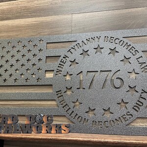 May include: A metal cutout of an American flag with a circle in the center that says "When Tyranny Becomes Law, Rebellion Becomes Duty" and "1776". The circle is surrounded by stars. The flag is made by "Big Dog Metalworks".