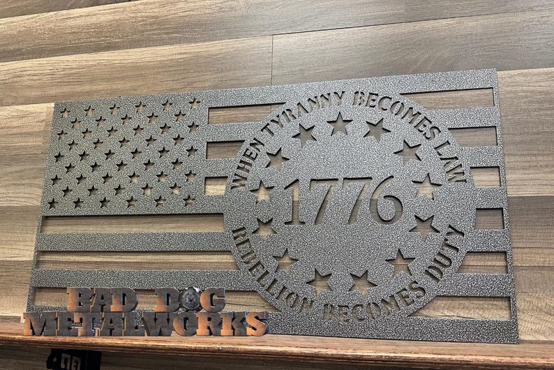 May include: A metal cutout of an American flag with a circle in the center that says "When Tyranny Becomes Law, Rebellion Becomes Duty" and "1776". The circle is surrounded by stars. The flag is made by "Big Dog Metalworks".