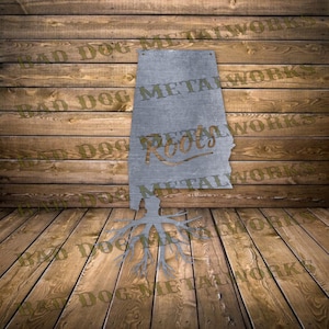 May include: Metal cutout of the state of Alabama with the word "Roots" in a stylized font. The cutout is attached to a wooden background and has a tree root design extending from the bottom.