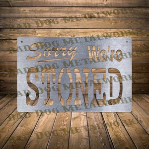 May include: A metal sign with the text "Sorry We're Stoned" in a distressed, vintage style. The sign is made of a silver metal and has a rustic look.