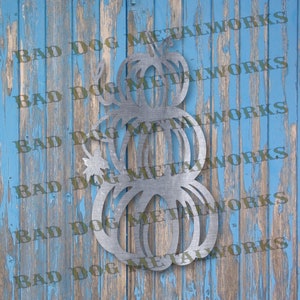 May include: A metal wall decor featuring three stacked pumpkins. The pumpkins are cut out of metal and have a rustic, weathered look.