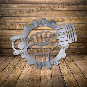 May include: A metal wall art piece featuring a gear with a fist holding a piston. The gear has the text "Bad Dog Metal Works" around the outside.