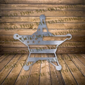 May include: A metal cutout of a sheriff's star with an American flag design. The star is silver and the flag is red, white, and blue. The star is on a wooden background.
