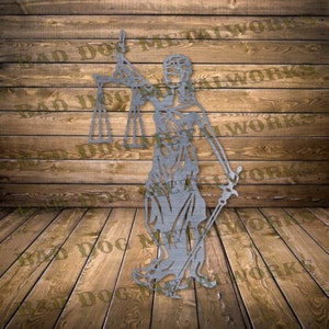 May include: A silver metal cutout of the figure of Lady Justice, holding a scale and a sword. The figure is standing on a wooden surface.