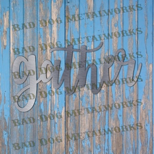May include: Metal wall decor with the word "gather" in a cursive font. The metal is a brushed silver color and has a rustic look. The background is a blue wooden wall.