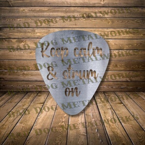 May include: A silver metal guitar pick with the text "Keep calm & strum on" cut out. The pick is on a wooden background.