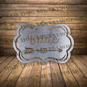 May include: A silver metal sign with a decorative border and the words "Bride to" with an arrow pointing to the right. The sign has a rustic, distressed look.