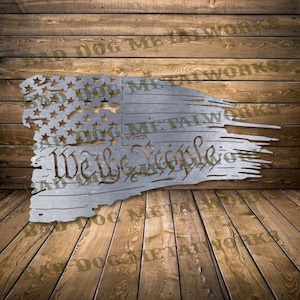 May include: A metal cutout of a distressed American flag with the words "We the People" in a script font. The flag is torn and tattered, with the stars and stripes visible.