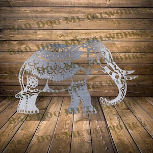 May include: A silver metal elephant silhouette with intricate cut-out designs. The elephant is standing on a wooden surface.