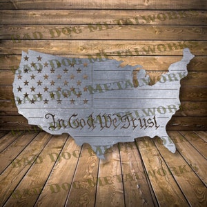 May include: A metal cutout of the United States of America with a star-spangled banner design and the words "In God We Trust" inscribed below. The cutout is on a wooden background.