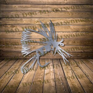 May include: A metal cutout of a fly fishing lure, with intricate details and a realistic design. The lure is made of silver metal and has a hook at the end. The background is a wooden wall.