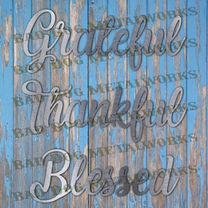 May include: Metal wall decor with the words "Grateful", "Thankful", and "Blessed" in a cursive script on a blue wood background.