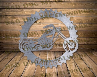 May include: A silver metal motorcycle silhouette is centered within a gear-shaped frame. The words "DAD'S GARAGE" and "BAD DOG METALWORKS" are cut into the metal. The motorcycle has a chopper style with a large front wheel.