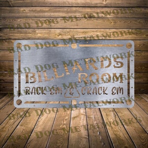 Könnte beinhalten: Ein silbernes Metallschild mit den Worten "Billiards Room" in goldener Schrift. Das Schild trägt außerdem den Text "Rack 'em & Crack 'em" in kleinerer Schrift. Das Schild befindet sich auf einem hölzernen Hintergrund.
