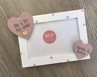 May include: White picture frame with pink polka dots and two pink heart-shaped wooden ornaments. The top ornament says "Me & My Big Sister" and the bottom ornament says "Carrie & Betsy".