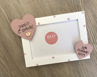 May include: White picture frame with pink polka dots and two pink heart-shaped decorations. The hearts have the text "Sarah's 1st Birthday" and "18th October 2019".