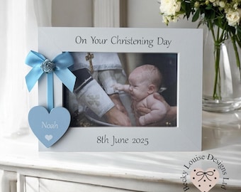 May include: A white photo frame with a baby baptism image. The frame has a blue bow and heart with the name "Noah". Text on the frame reads "On Your Christening Day" and "8th June 2025".