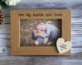 May include: A wooden photo frame with a light brown finish. The frame has a white heart-shaped plaque with the text "Love William x" on it. The frame has a photo of a young boy hugging a cat. The text "For My Auntie and Uncle" is printed on the top of the frame.