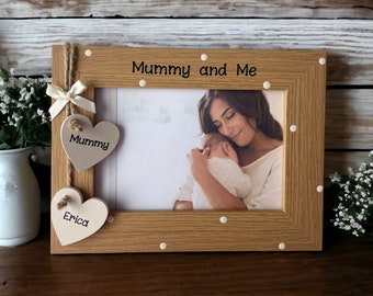 May include: A wooden photo frame with white polka dots and a white ribbon. The frame has two wooden hearts hanging from it, one that says "Mummy" and one that says "Erica". The frame says "Mummy and Me" at the top.