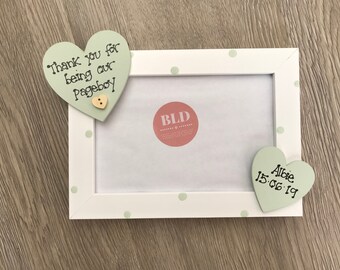 May include: White photo frame with green polka dots and two green heart-shaped wooden ornaments. The top ornament says "Thank you for being our Pageboy". The bottom ornament says "Albie 15.06.19".