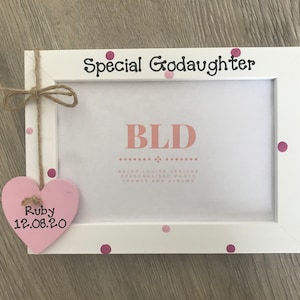 May include: White photo frame with pink polka dots and the text "Special Goddaughter" and "BLD Becky Louise Designs Personalised Photo Frames and Albums". A pink heart with the text "Ruby 12.08.20" is attached to the frame.