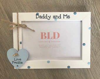 May include: White photo frame with blue polka dots and the text "Daddy and Me". A blue heart with the text "Love Freddie x" is hanging from the frame.