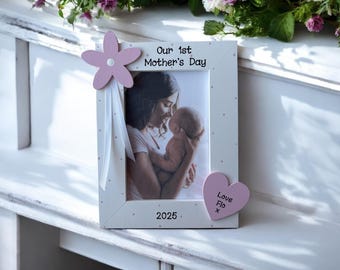 May include: White wooden photo frame with pink polka dots and a pink flower on the top left corner. The frame has a photo of a mother and child inside. The text "Our 1st Mother's Day 2025" is printed on the frame. A pink heart with the text "Love Flo x" is attached to the bottom right corner.