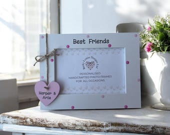 May include: A white photo frame with pink polka dots and the words "Best Friends" at the top. A pink heart-shaped tag hangs from the frame, with the names "Harper & Arlie" on it. The frame is personalized and handcrafted.