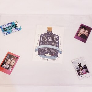 May include: A white card with a blue and purple bottle illustration and the text "There are big ships & small ships but the best ship of all is friendship". The card is surrounded by three Polaroid photos of two women and a photo of a building.