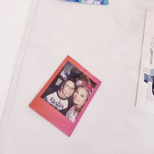 May include: A pink and white Polaroid photo of two women wearing mouse ears. The photo has the word "Besties" written on it. The photo is on a white background.