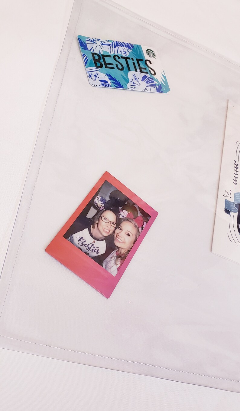 May include: A pink and white Polaroid photo of two women wearing mouse ears. The photo has the word "Besties" written on it. The photo is on a white background.