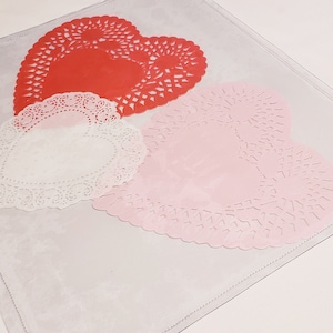 May include: Three heart-shaped paper doilies in red, white, and pink. The doilies are on a white surface.