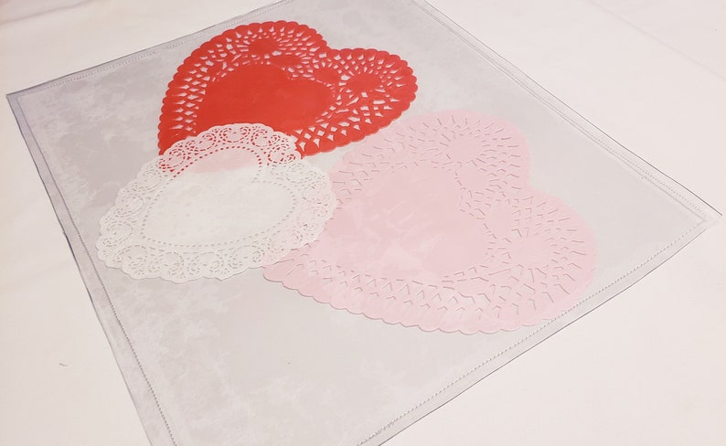 May include: Three heart-shaped paper doilies in red, white, and pink. The doilies are on a white surface.