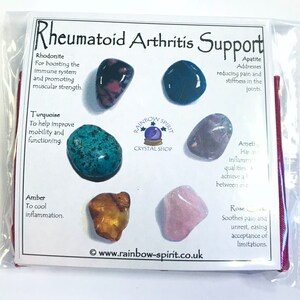 May include: A set of seven tumbled stones for rheumatoid arthritis support. The stones are rhodonite, turquoise, amber, amethyst, apatite, and rose quartz. The stones are arranged in a circle around a white card with the text "Rheumatoid Arthritis Support" and the name of each stone and its properties.