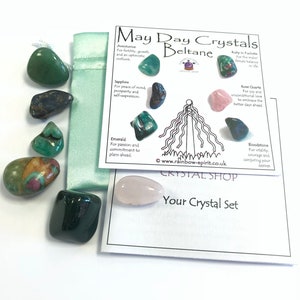 Pode incluir: Uma cole&ccedil;&atilde;o de pedras preciosas polidas em v&aacute;rias cores, incluindo verde, azul e rosa, juntamente com um cart&atilde;o com o texto "May Day Crystals Beltane". O conjunto inclui uma pequena bolsa verde e um cart&atilde;o descritivo.