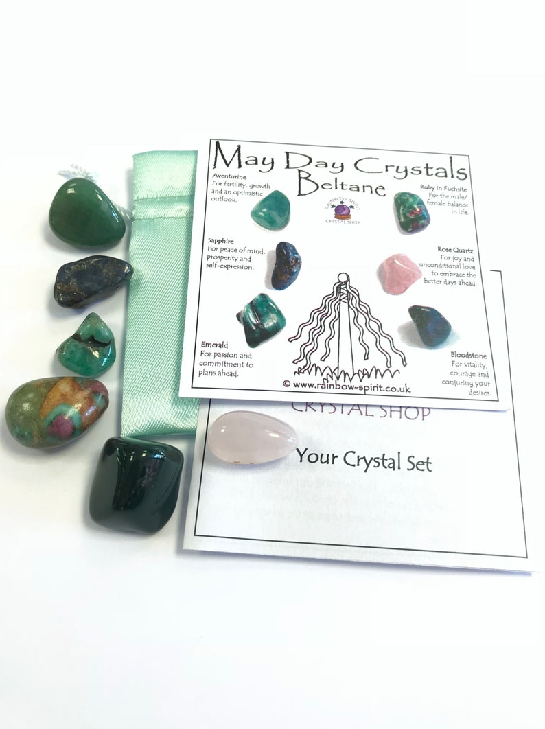 Pode incluir: Uma cole&ccedil;&atilde;o de pedras preciosas polidas em v&aacute;rias cores, incluindo verde, azul e rosa, juntamente com um cart&atilde;o com o texto "May Day Crystals Beltane". O conjunto inclui uma pequena bolsa verde e um cart&atilde;o descritivo.