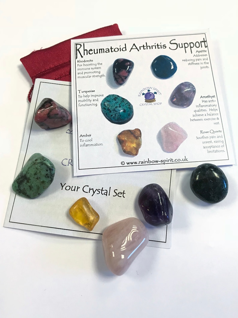 May include: A set of seven crystals for rheumatoid arthritis support. The crystals are rhodonite, turquoise, amber, amethyst, rose quartz, apatite, and green aventurine. The crystals are arranged on a white card with the text "Rheumatoid Arthritis Support" and "Your Crystal Set".