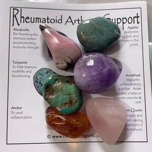 May include: Set of seven tumbled stones, including amethyst, rose quartz, turquoise, amber, apatite, rhodonite, and a green stone. The stones are arranged on a white card with text describing their properties for supporting rheumatoid arthritis.