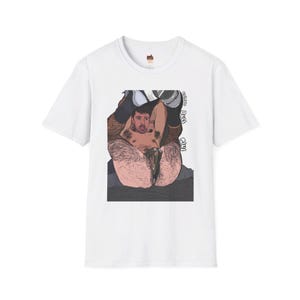 May include: White t-shirt with a black and white illustration of a man with a beard and mustache. The illustration is of the man sitting with his legs crossed and his arms around his legs. The text "Wonder Boy Extra" is printed on the shirt.