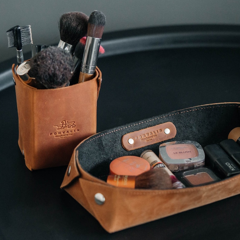 May include: A brown leather makeup organizer with the word "Ponyvalin" embossed on the front. The organizer is filled with makeup brushes and a small tray with makeup products.