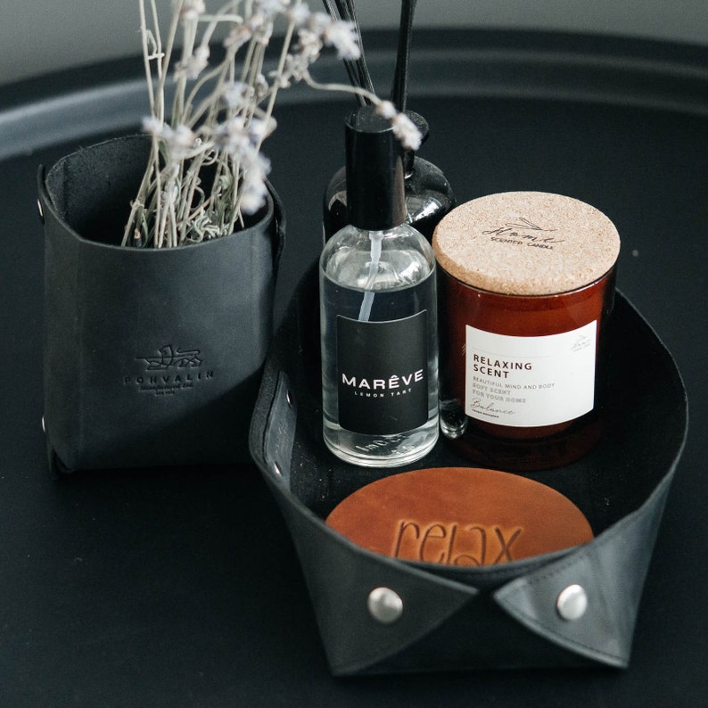 May include: A black leather tray with a brown leather coaster that says "relax" on it. There is a clear glass bottle of lemon tart scented room spray with a black label that says "Mar&egrave;ve Lemon Tart". There is also a brown glass candle with a cork lid that says "Relaxing Scent" and "Balance" on the label.