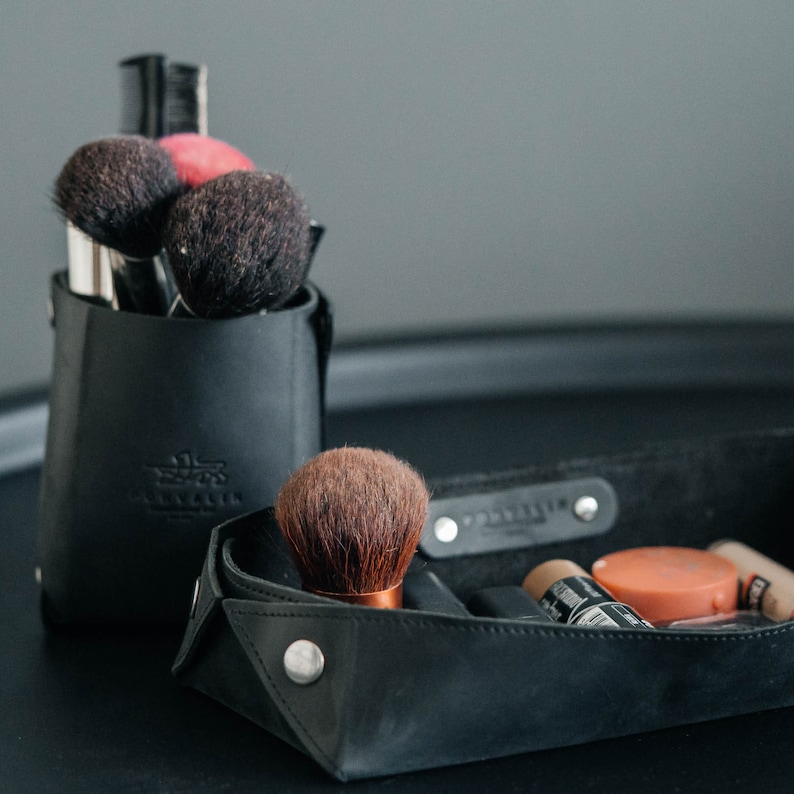 May include: A black leather makeup organizer with a variety of makeup brushes and a small tray for cosmetics. The organizer has a label that says "Traveler".
