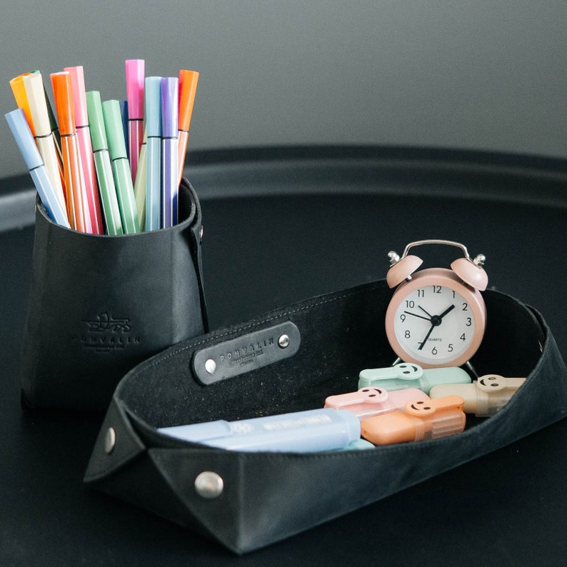 May include: A black leather tray with a pink alarm clock and colorful markers in a black leather cup. The tray has a label that says "Pommelier."