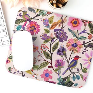 May include: A floral mouse pad with a pink, white, and green background. The mouse pad features a repeating pattern of colorful flowers and birds.
