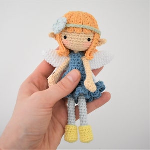 May include: A crocheted fairy doll with orange hair, a blue dress, white wings, and yellow shoes.